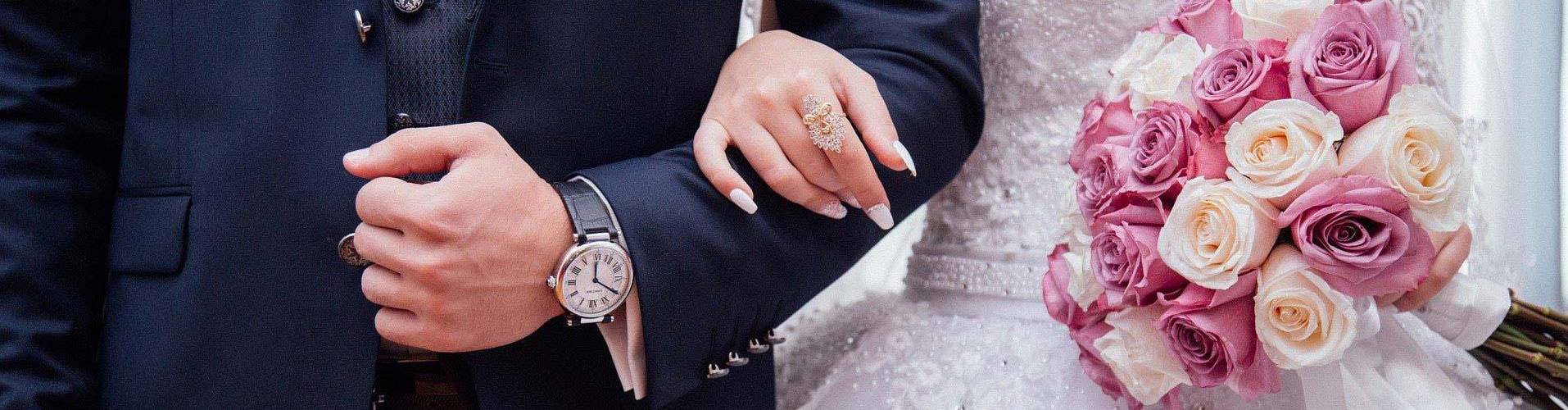 Hochzeitspaar hält sich am Arm mit Blumen